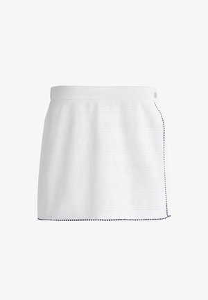Jupe blanche avec un tissage texturé, fente latérale et bordure bleu marine le long de l'ourlet, dotée d'une fermeture à bouton simple à la taille.