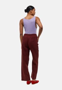 Débardeur lavande, associé à un pantalon bordeaux à jambes larges avec une taille élastique et des poches latérales. Des chaussures rouges complètent le look.