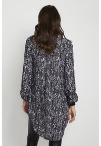 Tunique longue à manches longues noire à motifs floraux avec une coupe ample, présentant des motifs complexes en nuances de gris, blanc et touches de marron. Matière douce et fluide.