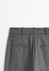Pantalons en laine gris avec une texture lisse, une taille plate, des passants de ceinture et deux poches arrière. Design simple adapté à diverses occasions.