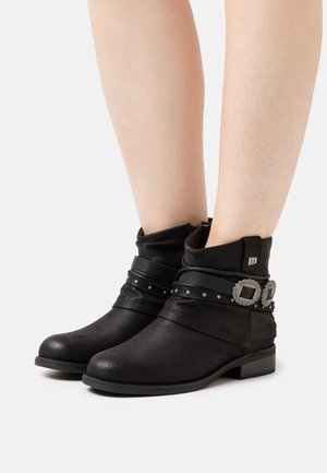 Black ankle boots with a slouch design, leather material, silver studs, two black straps with decorative buckles, and a low block heel.