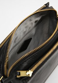 Czarna skórzana torba ze złotym suwakiem; wnętrze wyłożone szarą teksturowaną tkaniną i małą czarną metką. Otwiera się na przestronną komorę.