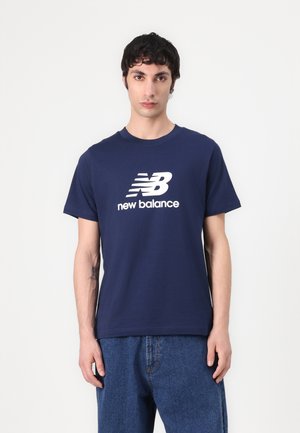 Navyblauwe katoenen T-shirt met een wit New Balance-logo, korte mouwen en een ronde hals, gecombineerd met blauwe spijkerbroek.