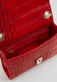 Borsa a mano in pelle rossa con una texture a motivo coccodrillo. L'interno presenta una tasca con zip e un scomparto, con chiusura in hardware dorato.