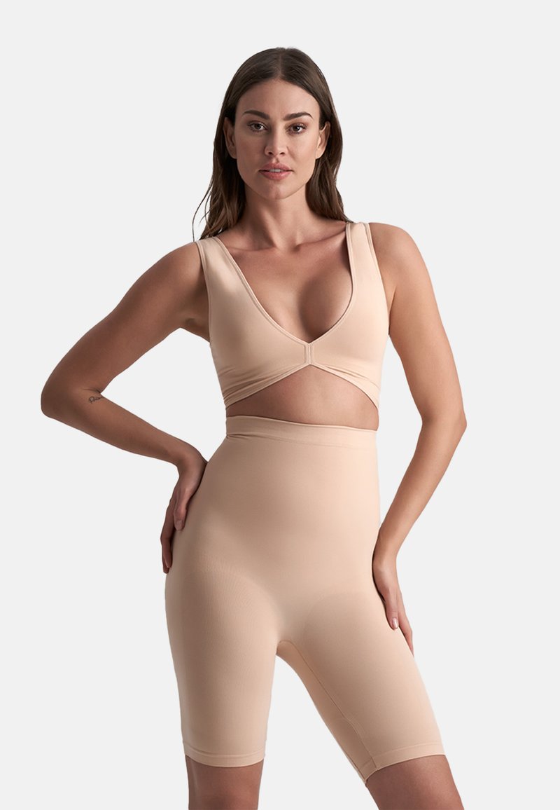 Set di abbigliamento attivo seamless color nude, composto da un reggiseno sportivo con scollatura a V e pantaloni corti a vita alta, caratterizzati da una texture liscia e un design aderente.