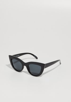 Lunettes de soleil noires en forme de œil de chat avec des verres foncés, une monture en plastique brillant et des bords angulaires. Marque visible sur la branche gauche.