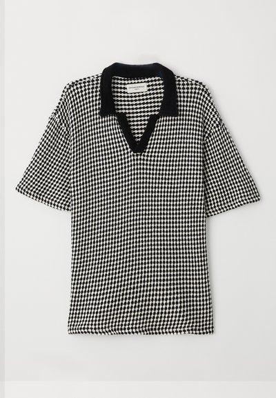 Polo de color negro y blanco con un patrón de cuadros, escote en forma de V y cuello negro en contraste. Las mangas cortas y amplias ofrecen un ajuste relajado.