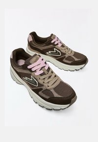 Chaussures de course en mesh marron et beige avec des semelles blanches épaisses, des lacets roses et beiges, et un logo blanc stylisé sur le côté.