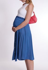 Jupe en jean bleu avec des boutons, design plissé et taille élastique ; associée à un crop top blanc ajusté et un petit sac à main rouge.