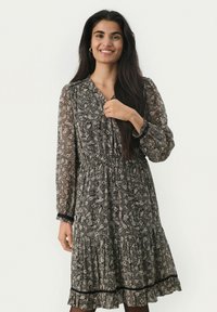 Zwart-witte bloemenprint jurk met lange mouwen, een losse pasvorm, een gathered taille en een gerimpelde zoom. Doorzichtig stof met zwarte randdetails.