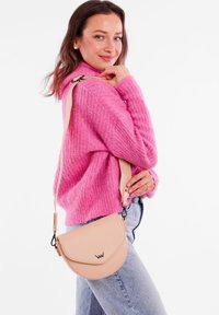 Béžová taška přes rameno s kulatým uzávěrem, kožený materiál, nastavitelný popruh a decentní detail loga značky.