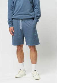 Blauwe katoenen shorts met een elastische tailleband en witte trekkoord, voorzien van zijzakken en subtiele branding op het linkerbeen.