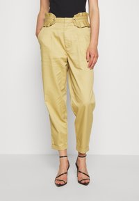 Pantalons beiges taille haute avec ceinture plissée et volants, boutons sur les côtés ; coupe ajustée aux chevilles ; tissu lisse et léger.