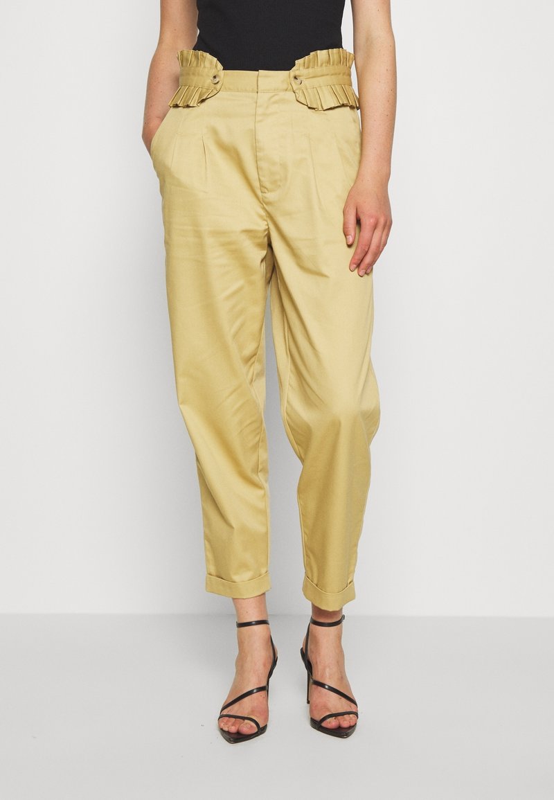 Pantalons beiges taille haute avec ceinture plissée et volants, boutons sur les côtés ; coupe ajustée aux chevilles ; tissu lisse et léger.