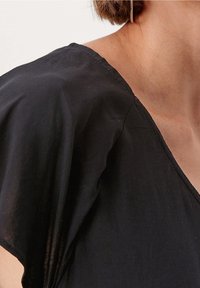 Top nero, leggero, con scollatura a V e maniche corte. Il tessuto appare liscio con una leggera lucentezza. Le cuciture sono ordinate e uniformi.