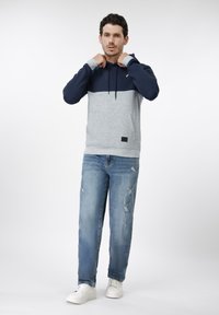 Φούτερ με κουκούλα σε ναυτικό μπλε και ανοιχτό γκρι με υφασμένο σχέδιο και μπροστινή τσέπη. Συνδυασμένο με μπλε τζιν με ξεφτίσματα και λευκά αθλητικά παπούτσια.