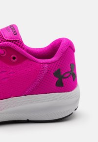 Chaussure de sport en mesh rose avec un design texturé, logo de marque noir et semelle blanche. Couture détaillée le long du talon et des œillets.