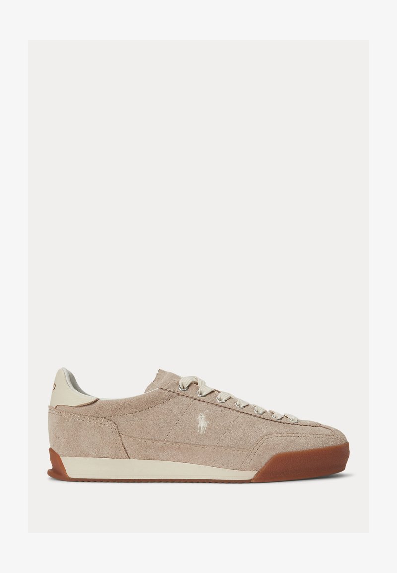 Baskets basses en daim beige avec des lacets blancs, un logo blanc sur le côté et une semelle en caoutchouc marron.