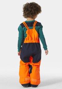 Oranžový a námořnický modrý nepromokavý sněhový oblek s nastavitelnými popruhy, širokými nohavicemi a suchým zipem na kotnících. Obsahuje lehký izolační materiál.