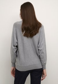 Pull gris surdimensionné en tissu doux. Comprend des manches amples, un ourlet côtelé et une coupe décontractée, contrastant avec un jean foncé.