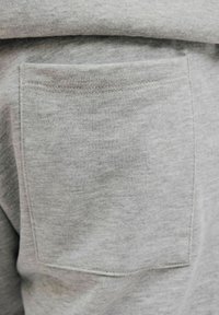 Gros plan sur une poche plaquée en tissu gris clair cousue sur un tissu de sweat-shirt assorti avec des coutures visibles autour des bords.