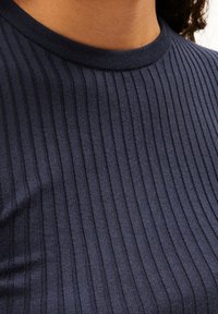 Granatowa, prążkowana bluzka z okrągłym dekoltem, o miękkiej teksturze i równomiernie rozmieszczonych pionowych liniach, podkreślająca dopasowany krój.