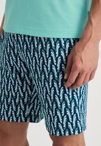 Pantaloni da nuoto blu navy con un motivo ondulato bianco e verde. Il materiale sembra leggero con una texture morbida.