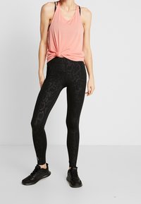 Růžový tílko zavázané v pase, kombinované s vysokým pasem černých legín s hadím potiskem a černými sportovními botami.