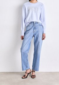 Ljusblå sweatshirt med "DKNY" i glitter, kombinerad med högmidjade ljusblå jeans. Modellen bär svarta klackar med remmar.