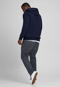 Marineblaues Kapuzenshirt mit verstellbarem Kordelzug, kombiniert mit strukturierten grauen Hosen mit dezentem Muster und weißen Sneakern.