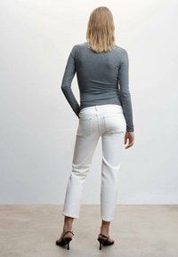 Camiseta gris de mangas largas, jeans blancos de corte recto, ajuste slim, textura suave. Sandalias de tacón negras, vista desde atrás sobre un fondo claro.