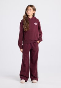 Burgundy hoodie and wide-leg sweatpants set. Hoodie has a front pocket and logo; pants feature white side stripes and a relaxed fit.