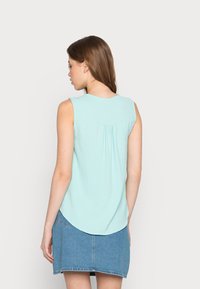 Top sem mangas azul claro com decote redondo, tecido texturizado e detalhe de costas franzidas, combinado com uma saia de ganga.