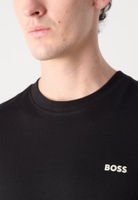 Juoda medvilninė marškinėliai su apvaliu iškirpimu, ant kairės krūtinės pusės esančiu baltu "BOSS" logotipu. Lygi tekstūra, prigludusi forma.