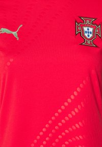 Crvena sportska majica s teksturiranom završnom obradom i gradijentnim uzorkom, zeleni Puma logo i izvezeni grb Portugala s složenim detaljima.