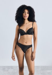 Čierna čipková podprsenka a zodpovedajúce tangá so zvlnenými okrajmi. Podprsenka má vystužené košíčky a nastaviteľné ramienka. Hladká, jemná textúra.