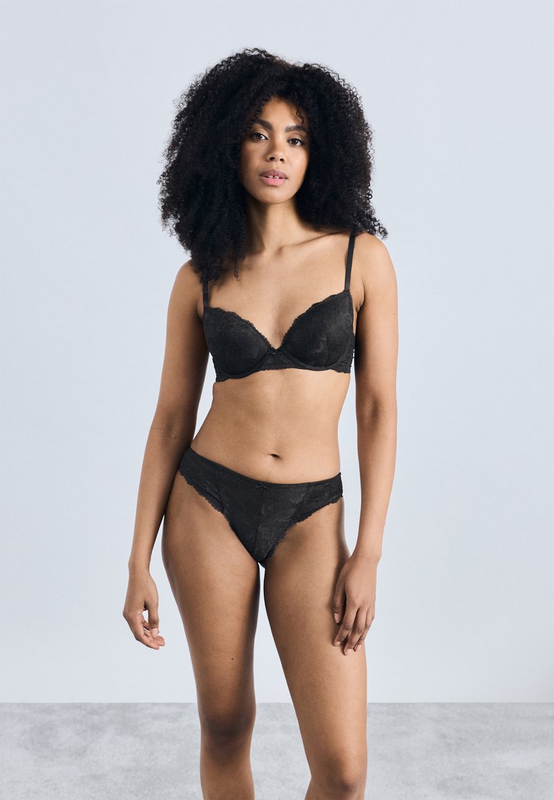 Čierna čipková podprsenka a zodpovedajúce tangá so zvlnenými okrajmi. Podprsenka má vystužené košíčky a nastaviteľné ramienka. Hladká, jemná textúra.