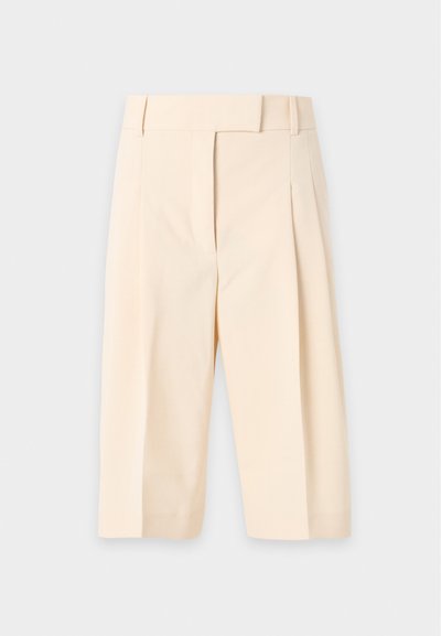 Pantalon cropped beige taille haute avec passants de ceinture, plis à l'avant et fermeture avant dissimulée.