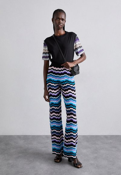 Γυναικείο μαύρο τοπ και παντελόνι με σχέδιο κυμάτων σε μπλε, μωβ και ροζ. Συνδυάζεται με μία μικρή μαύρη τσάντα και υποδήματα.