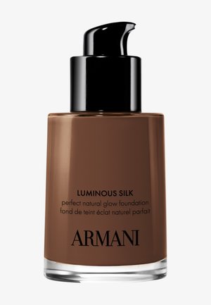 Flacon de fond de teint en verre brun avec un bouchon-pompe noir, étiqueté "Luminous Silk" et "fond de teint éclat naturel parfait" en lettres claires.