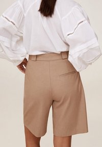 Vaaleanbeiget, räätälöidyt shortsit, joissa sileä pinta, takatasku ja vyötärönauha. Yhdistetty valkoiseen puseroon, jossa on liehupusut.