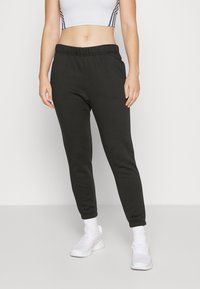 Svarta träningsbyxor av mjukt material, med resårmidja och smalnande muddar, i kombination med vita sportskor.