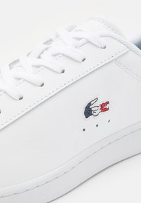 Sneaker in pelle bianca con punta rotonda, lacci piatti e logo ricamato. Presenta cuciture di accentuazione verdi e piccole perforazioni per traspirabilità.