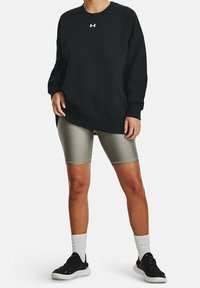 Sudadera negra con cuello redondo y logotipo blanco, combinada con pantalones cortos de bicicleta en un tono oliva claro. Zapatillas negras con suelas blancas y calcetines.