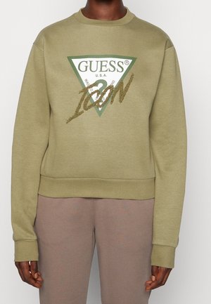 Olivgrön sweatshirt med rund halsringning, prydd med en triangulär logotyptryck i vitt och grönt, accentuerad av glittrande guldtext.