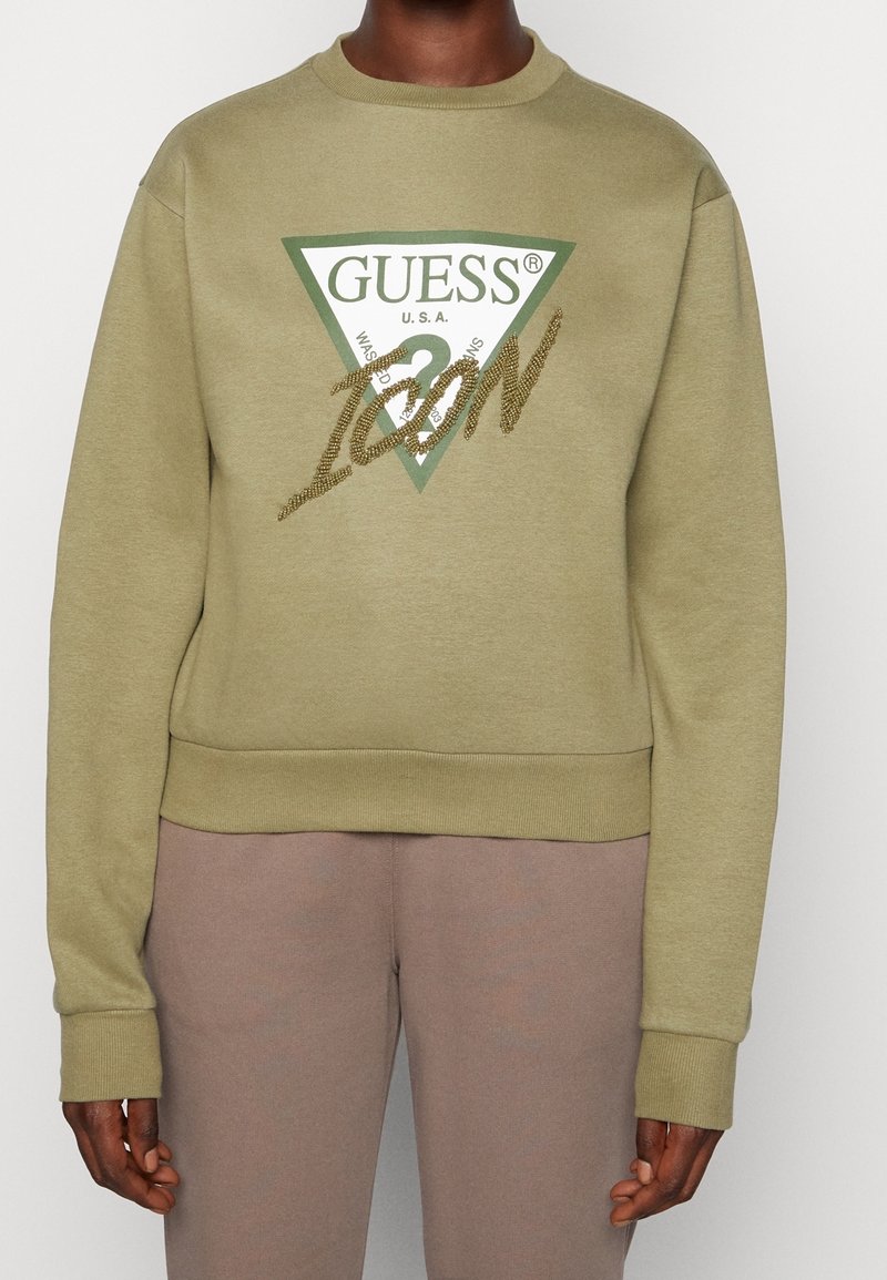 Sudadera verde oliva con cuello redondo, que presenta un estampado de logo triangular en blanco y verde, acentuado por letras doradas brillantes.