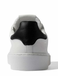 Sneaker bianco con un accento in pelle nera sul tallone, caratterizzato da una texture liscia e una suola bianca spessa. Design minimalista, linee pulite.