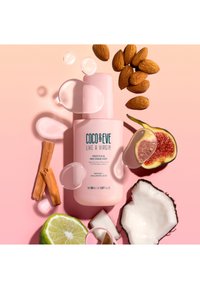 Rosa flaska med hårmist och pumpkork, omgiven av kokos, lime, fikon-skivor, mandlar och vattendroppar på en rosa bakgrund.