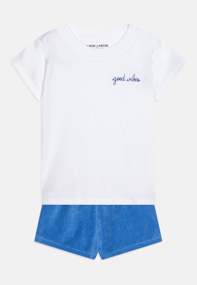 T-shirt blanc à manches courtes avec texte "good vibes" en bleu sur la poitrine, associé à un short bleu sur un fond uni.