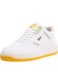 White sneaker with yellow rubber sole, visible perforations, green and purple accents, and a yellow smiley face logo on the tongue.